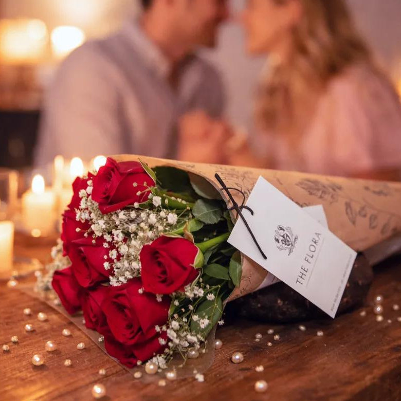 valentine day
Bouquet of red roses with a 'The Flora' tag on a wooden table, with a couple in the background.