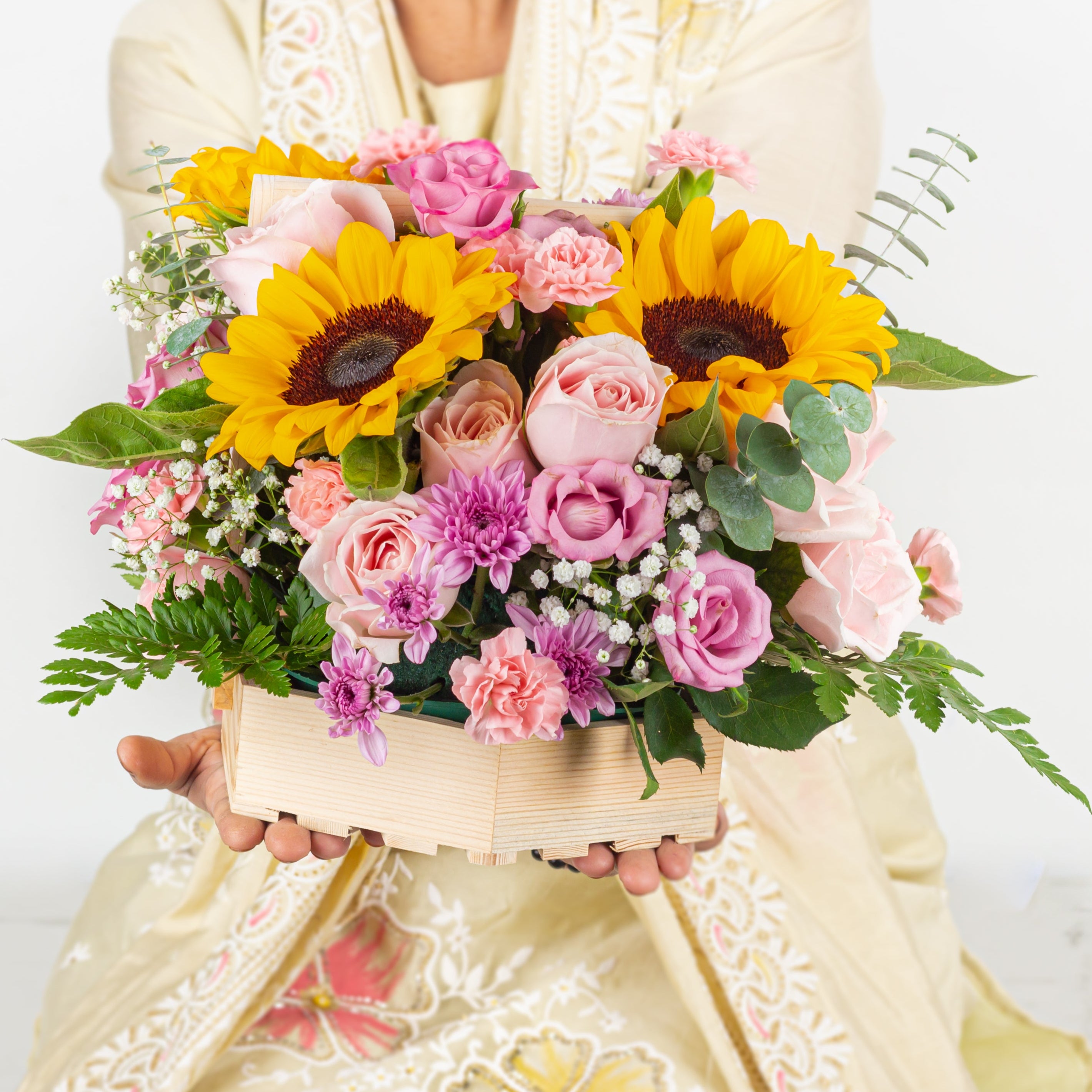 Person holding a bouquet of flowers with sunflowers and pink roses on a light background
