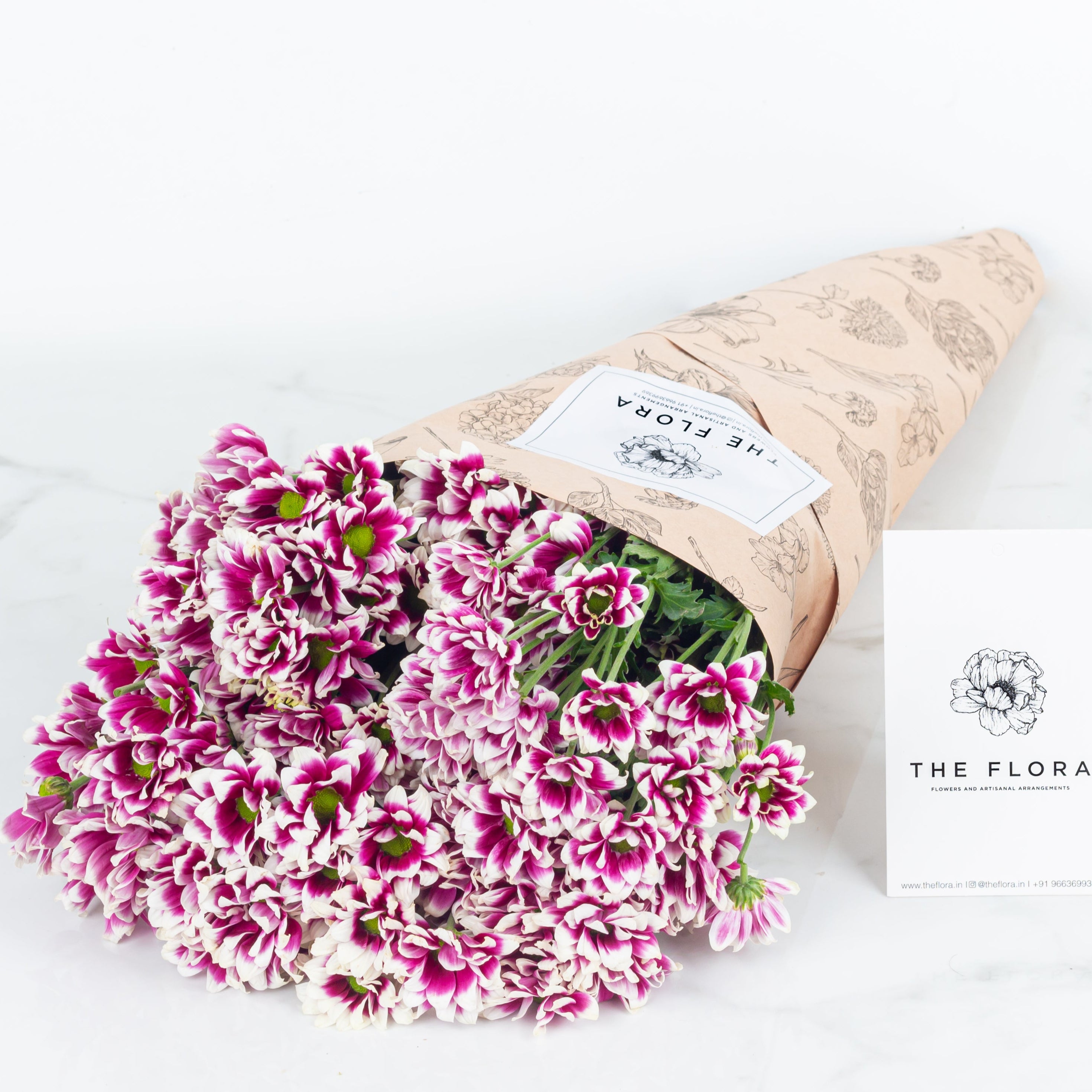 Bouquet of pink and white Santini Chrysanthemums wrapped in brown paper with 'The Flora' card. Online cut flowers with same day delivery at www.theflora.in