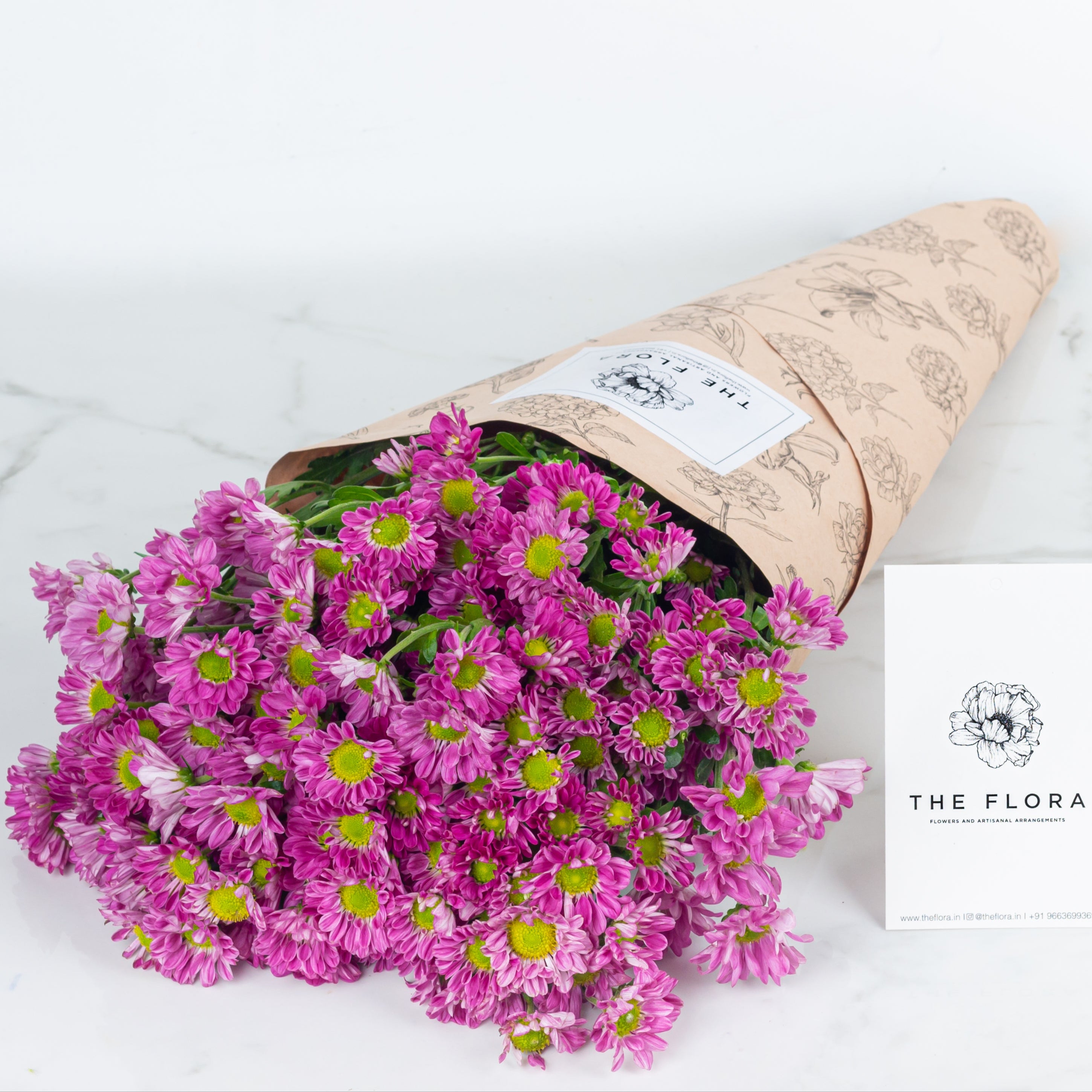 Bouquet of pink flowers Santini Chrysanthemums wrapped in brown paper with 'The Flora' logo. Online cut flowers n sustainable packaging from www.theflora.in