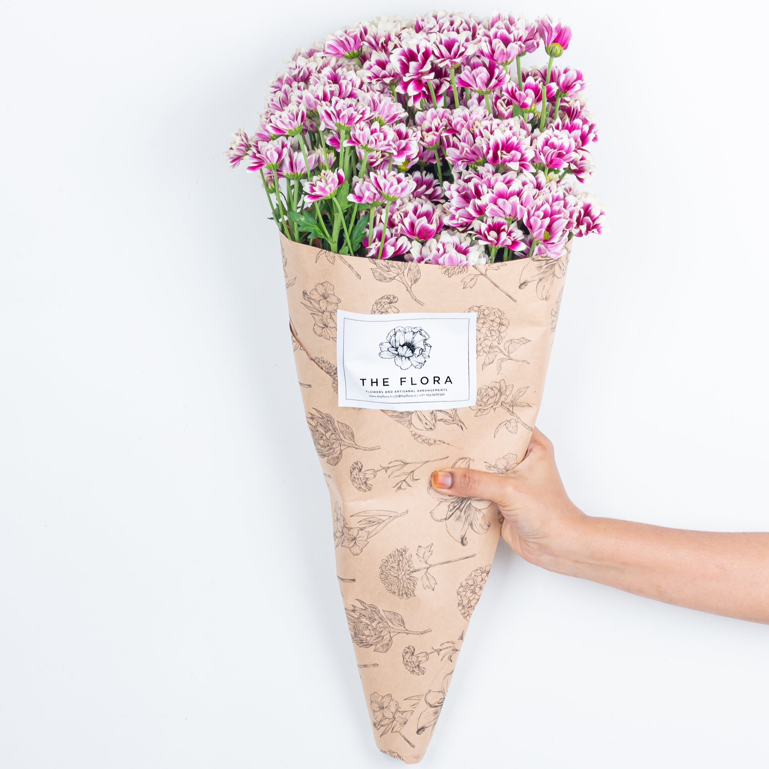 Bouquet of pink Santini Chrysanthemums wrapped in paper with 'The Flora' sticker. Online cut flowers with same day delivery at www.theflora.in
