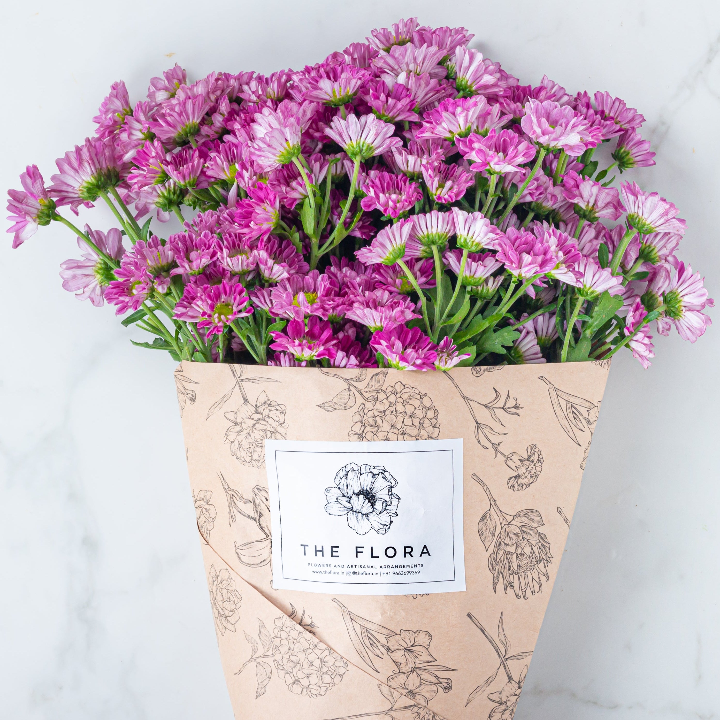 Bouquet of pink flowers Santini Chrysanthemum wrapped in brown paper with 'The Flora' label. Online cut flowers n sustainable packaging from www.theflora.in