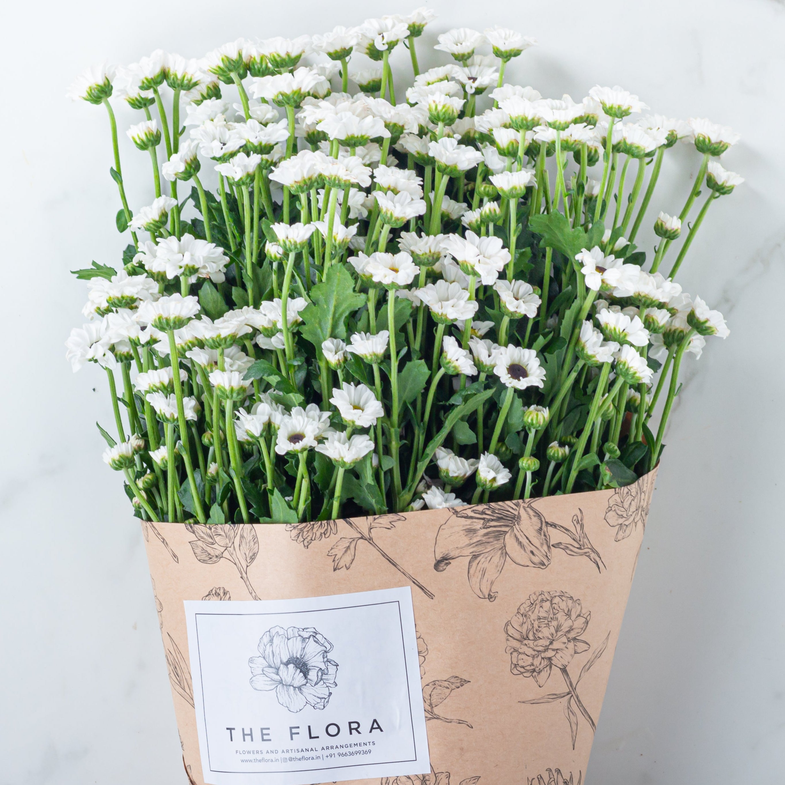 Bouquet of white flowers Santini Chrysanthemum wrapped in brown paper with floral patterns. Online cut flowers n sustainable packaging from www.theflora.in