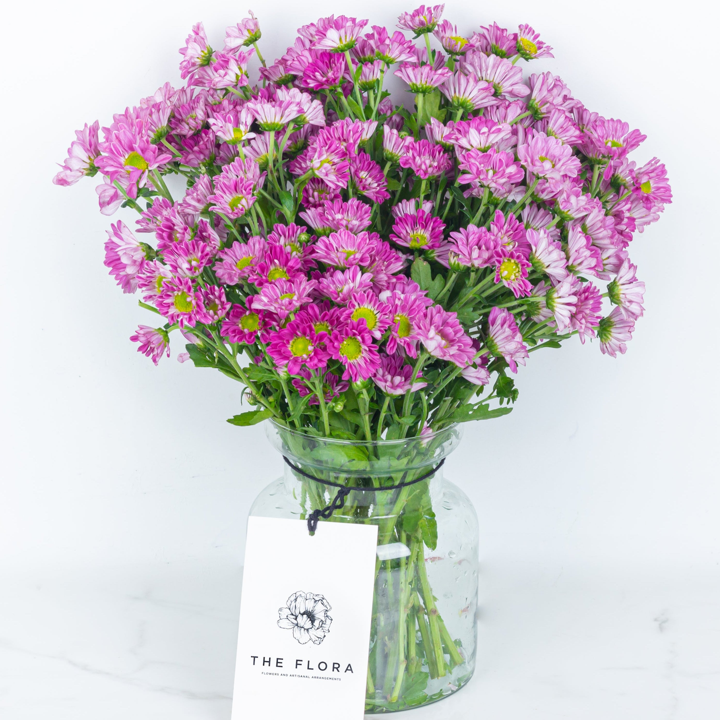 Bouquet of pink flowers Santini Chrysanthemums in a clear vase with 'The Flora' tagOnline cut flowers n sustainable packaging from www.theflora.in