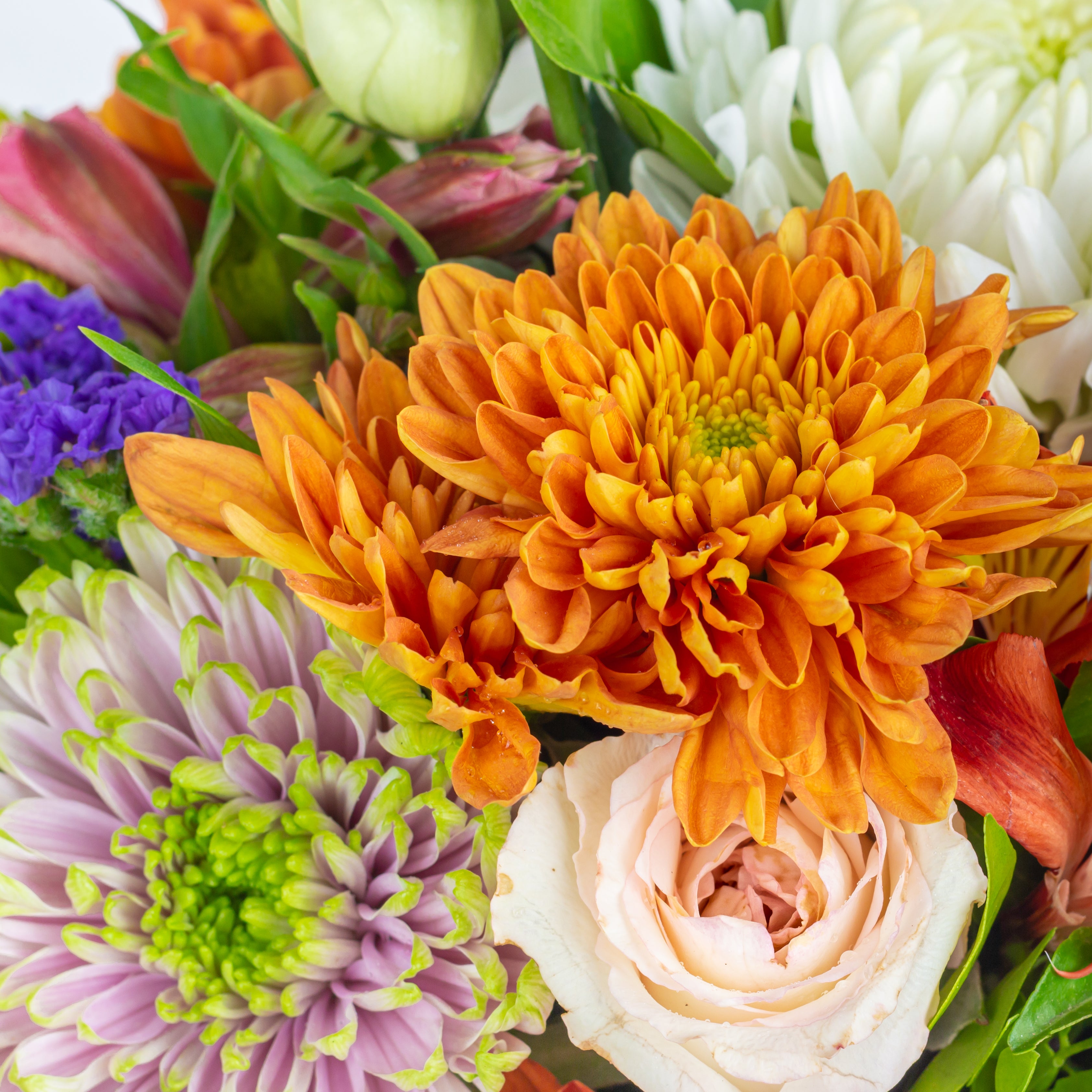 close up of a Bouquet of colorful flowers including orange, purple, and white. called Guardian Grace with Alstroemeria, Lisianthus , Disbud Chrysanthemums, Blue Statice and Roses. Online artisanal bouquets with same day delivery in sustainable packaging at www.theflora.in