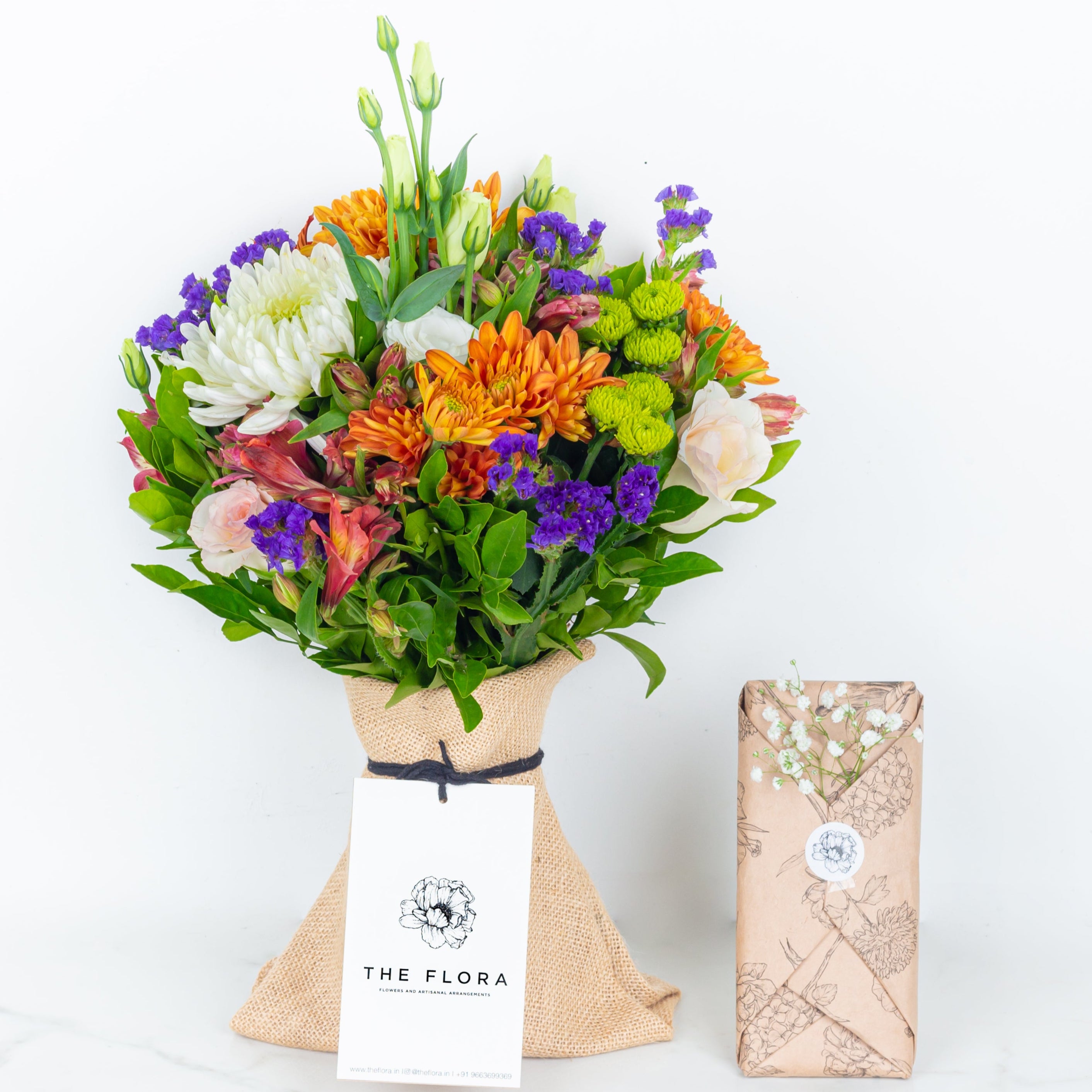 Colorful bouquet of flowers with 'The Flora' branding on a white background Colorful bouquet of flowers wrapped in paper with 'The Flora' label called Guardian Grace with Alstroemeria, Lisianthus , Disbud Chrysanthemums, Blue Statice and Roses. Online artisanal bouquets with same day delivery in sustainable packaging at www.theflora.in