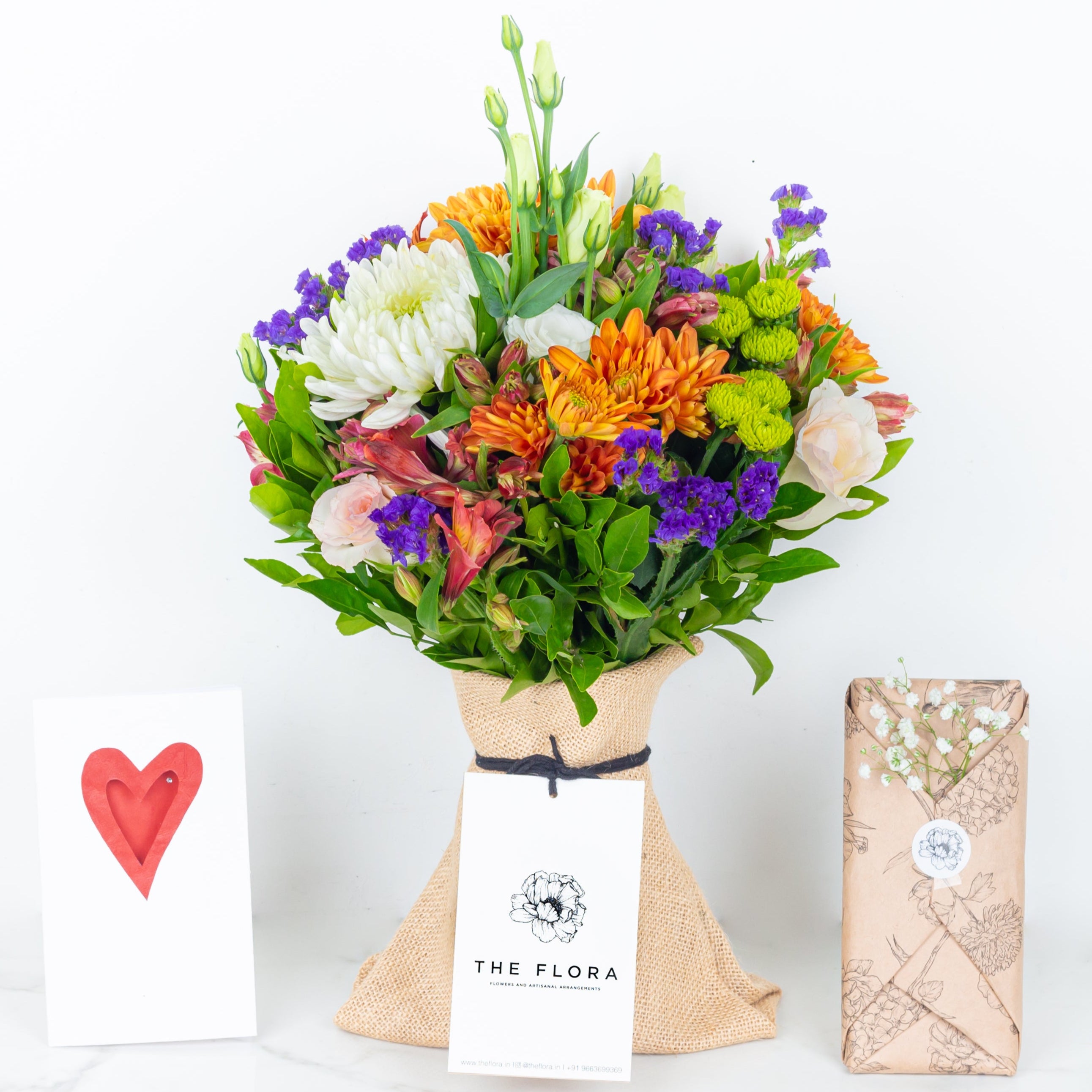 Colorful bouquet of flowers wrapped in paper with a card and chocolates Guardian Grace bouquet with Alstroemeria, Lisianthus , Disbud Chrysanthemums, Blue Statice and Roses. Online artisanal bouquets with same day delivery in sustainable packaging at www.theflora.in