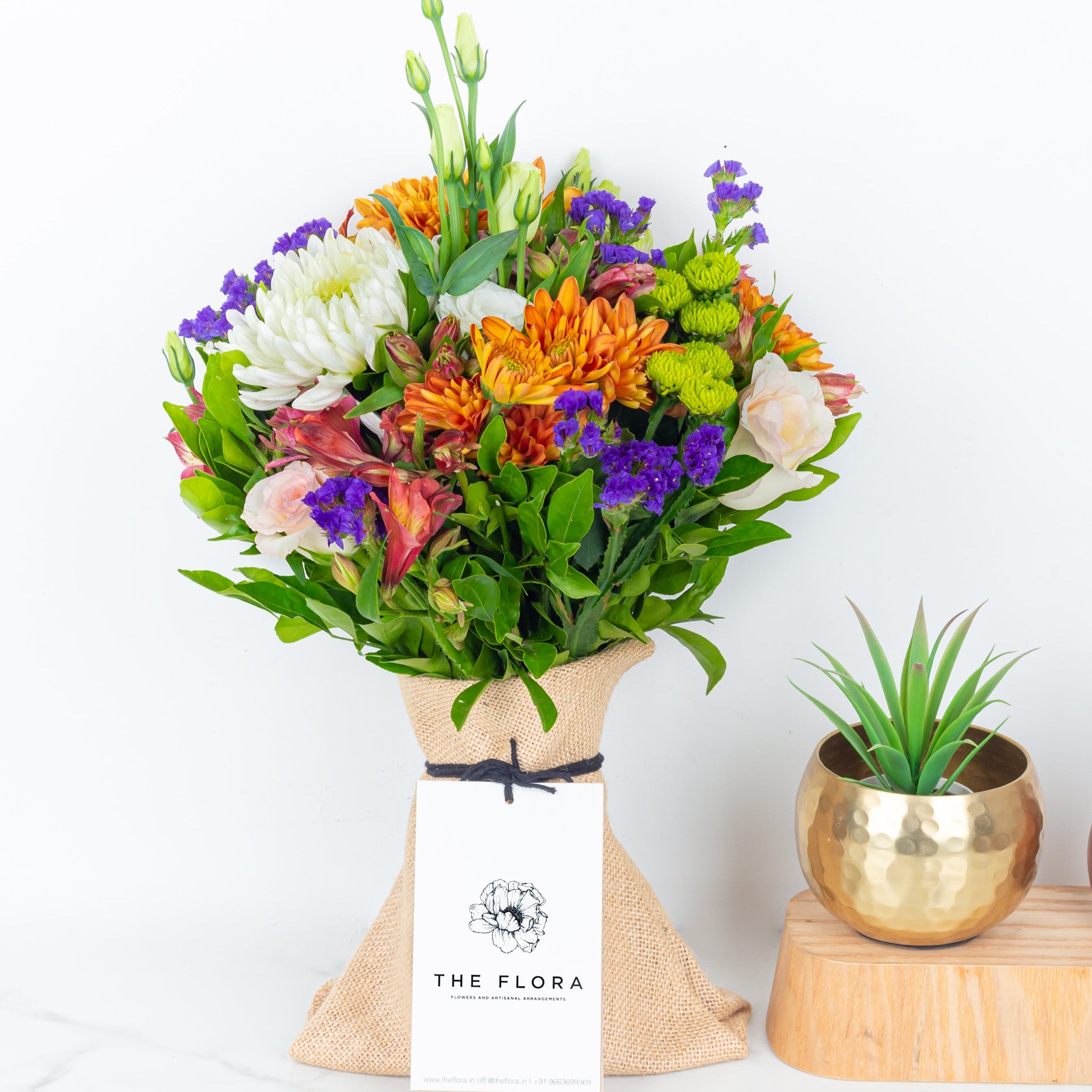 Colorful bouquet of flowers wrapped in burlap with 'The Flora' label called Guardian Grace with Alstroemeria, Lisianthus , Disbud Chrysanthemums, Blue Statice and Roses. Online artisanal bouquets with same day delivery in sustainable packaging at www.theflora.in