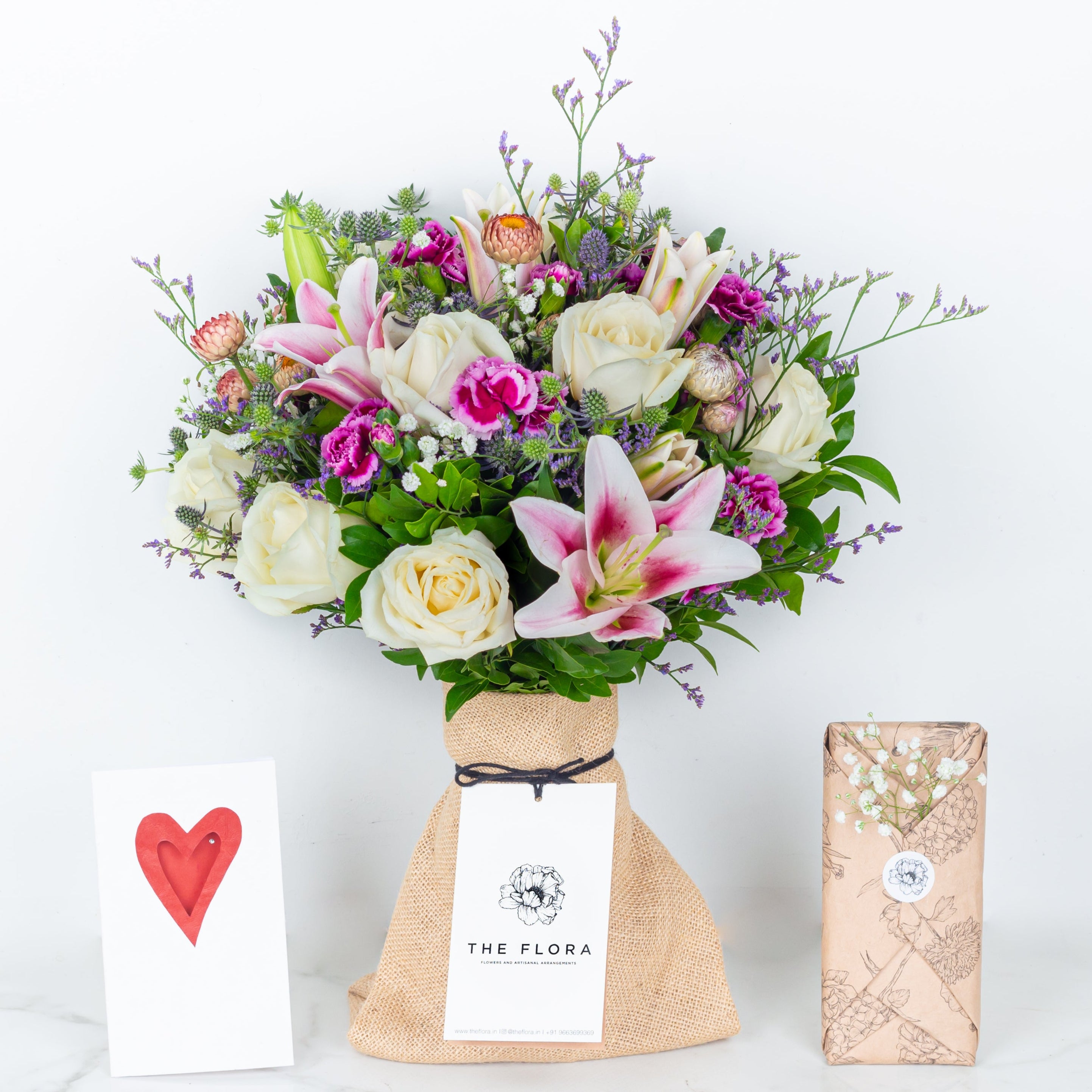 Bouquet of flowers as a gift in a paper bag called Soulful Strings with card and chocolates wrapped in the flora style. An artisanal bouquet of Eryngium, Roses, Oriental Lilies Helichrysum, Spray Carnations. and Limonium. Online artisanal bouquets with same day delivery at www.theflora.in