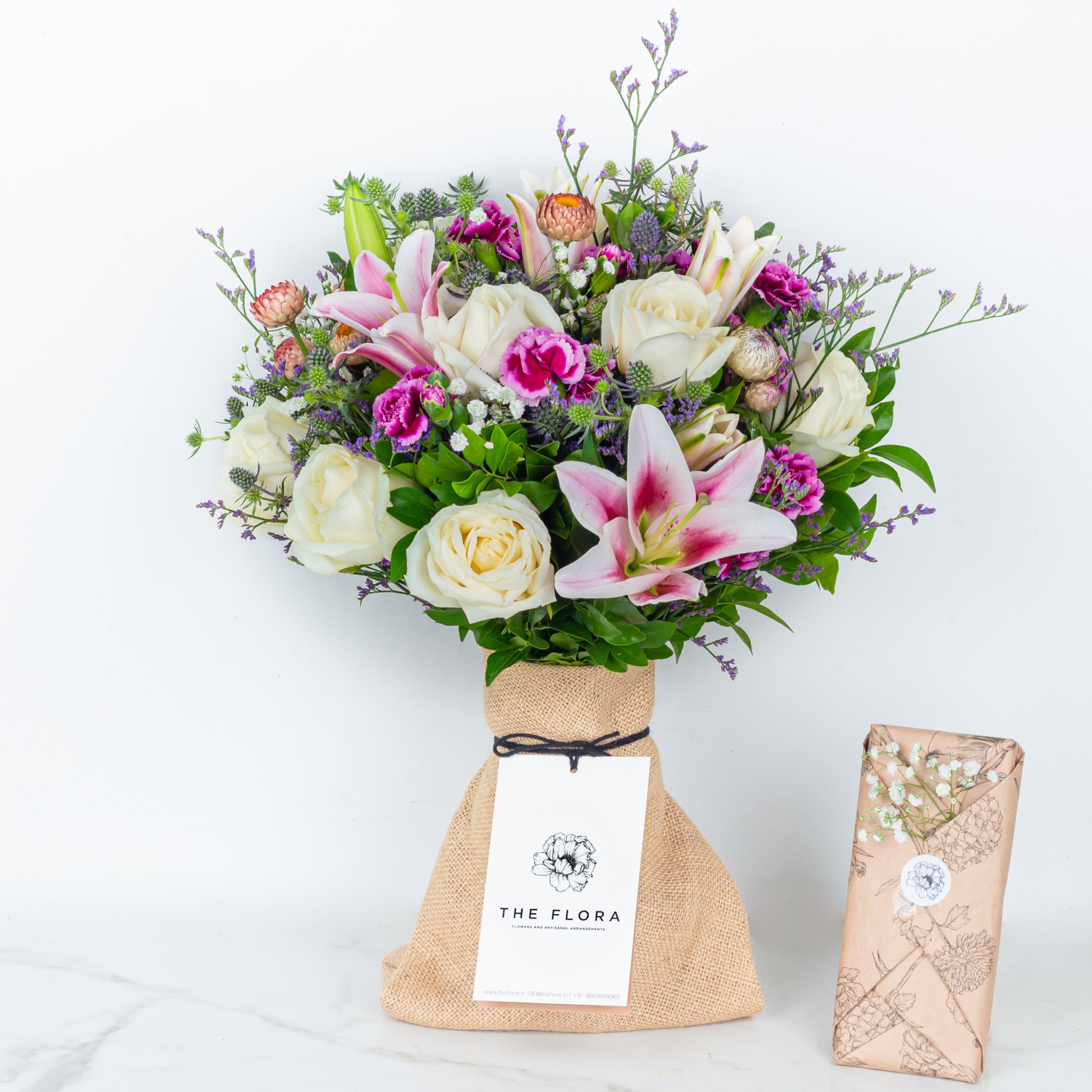 Bouquet of flowers as a gift in a paper bag called Soulful Strings with chocolates wrapped in the flora style. An artisanal bouquet of Eryngium, Roses, Oriental Lilies Helichrysum, Spray Carnations. and Limonium. Online artisanal bouquets with same day delivery at www.theflora.in