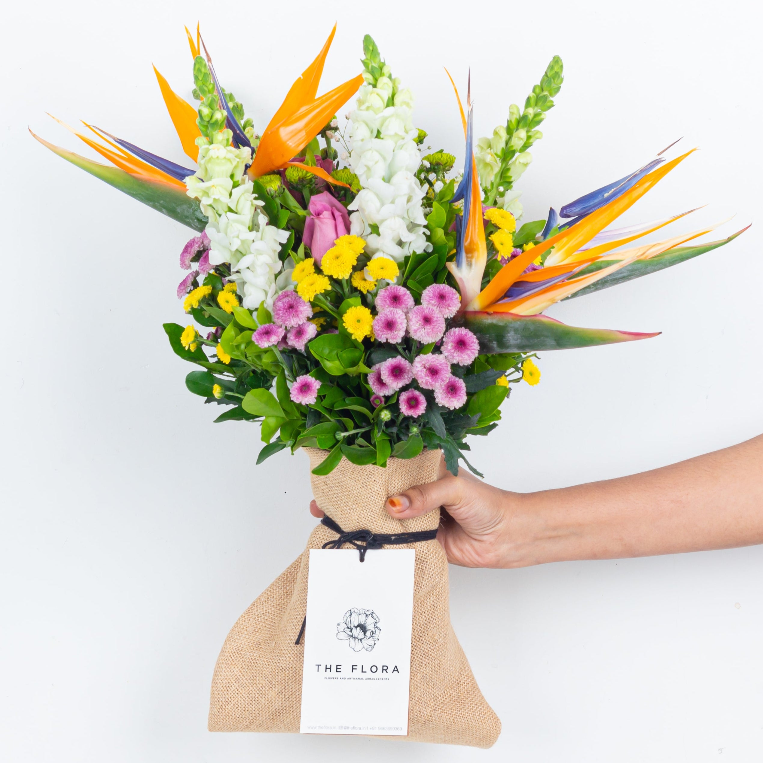 Bouquet of colorful flowers held by a person With All My Heart, an artisanal bouquet curated with Birds of Paradise, Button Chrysanthemums and roses. Online artisanal bouquets with same day delivery in sustainable packaging at www.theflora.in