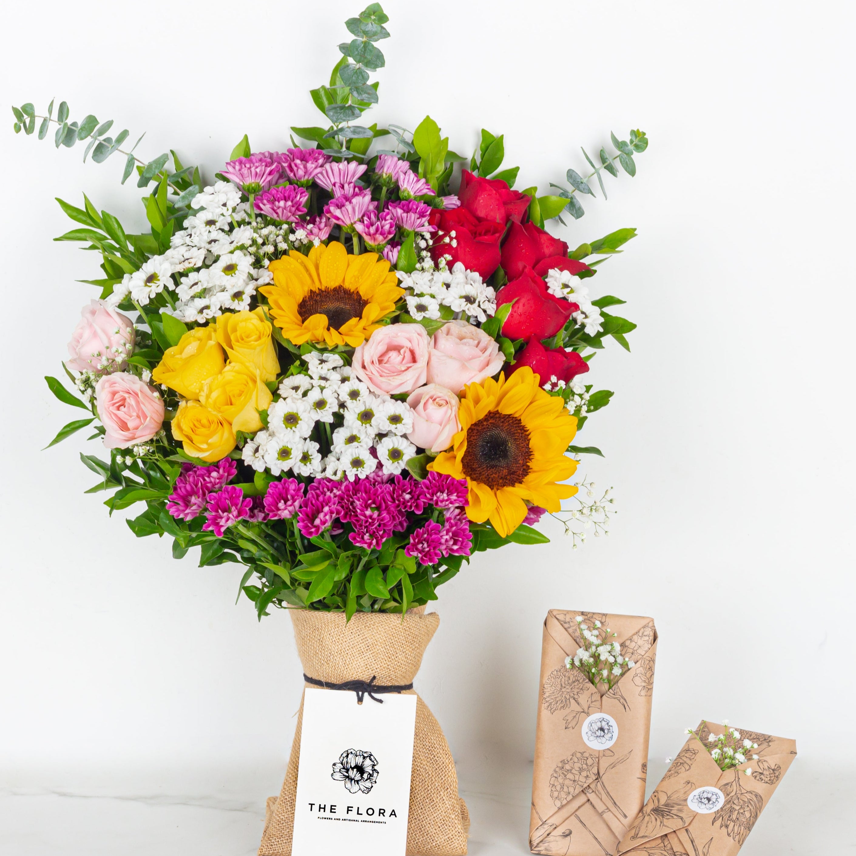 Colorful bouquet of flowers in a paper bag with 'The Flora' label on a white background