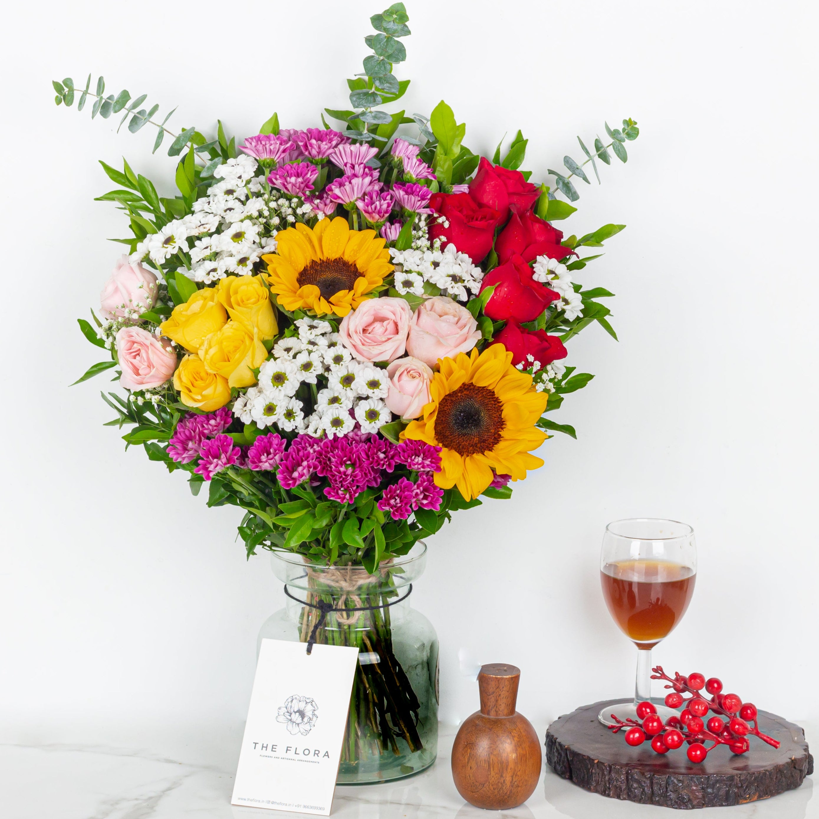 Bouquet of flowers with a glass of wine and a small vase on a white surface