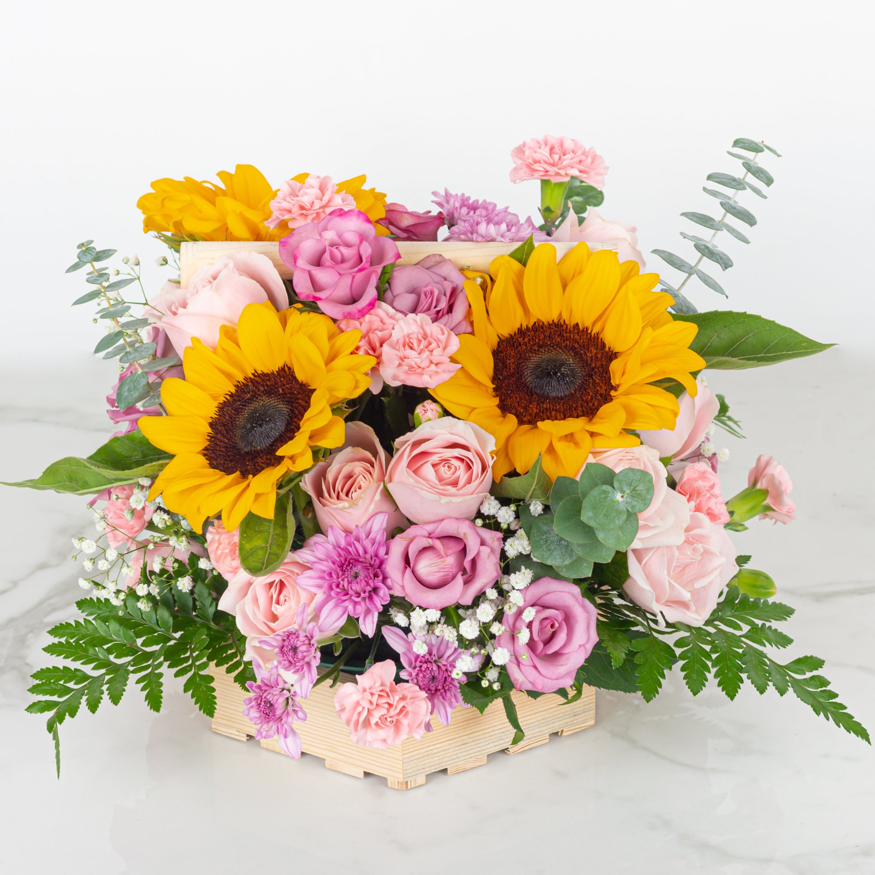 Colorful flower arrangement with sunflowers and pink roses in a wooden crate on a white background