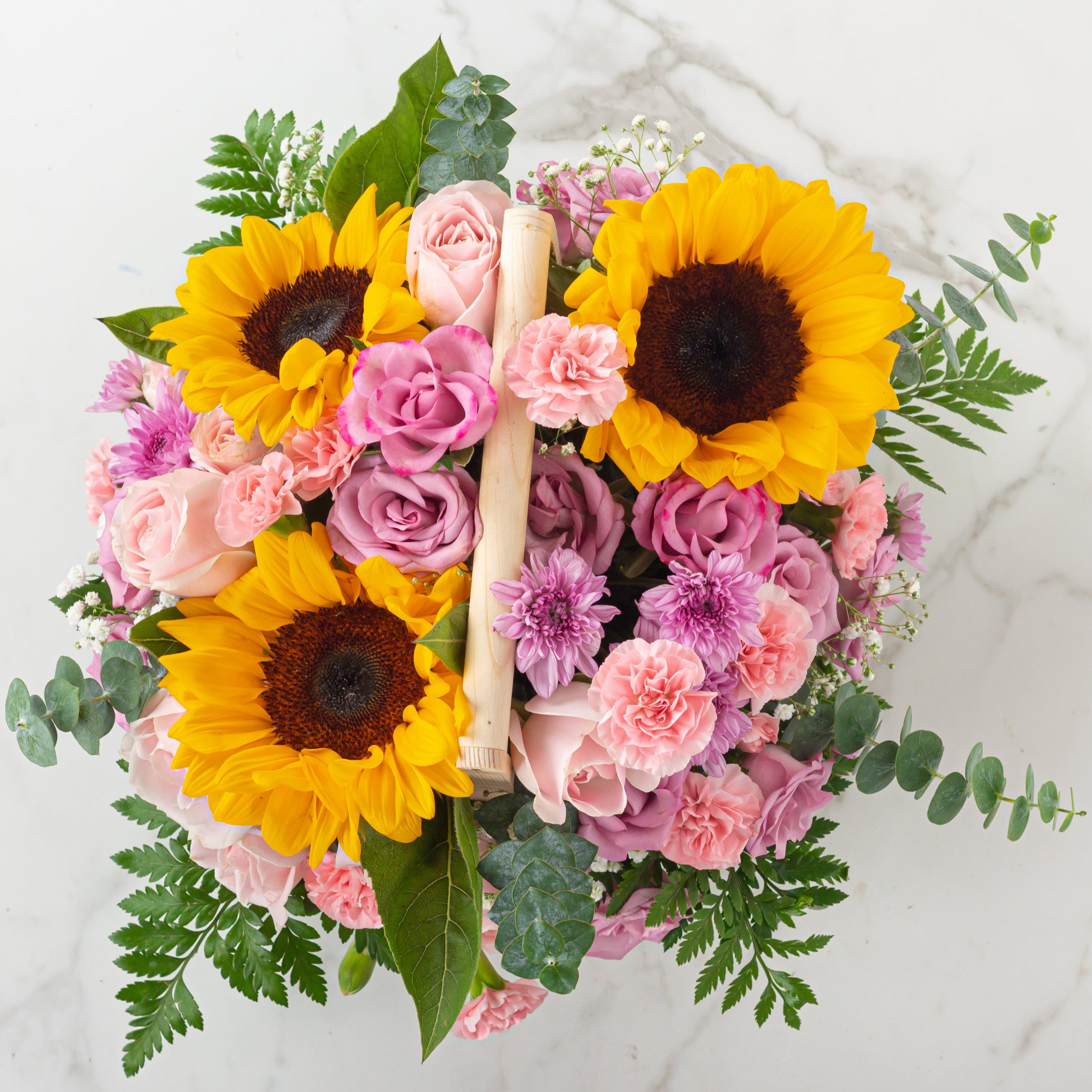 Floral arrangement with sunflowers and pink roses in a basket on a marble surface