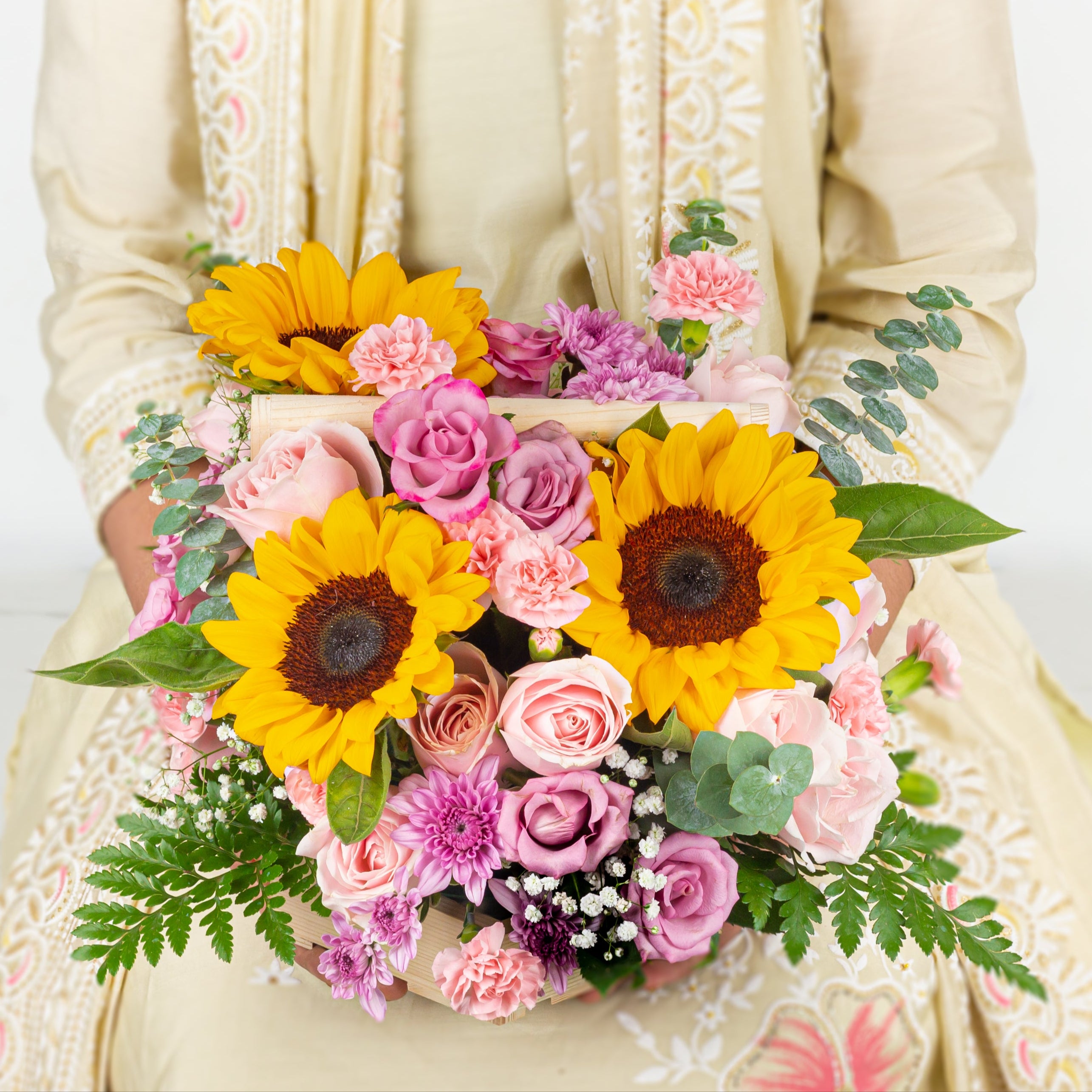 Person holding a bouquet of flowers with sunflowers and pink roses on a white background