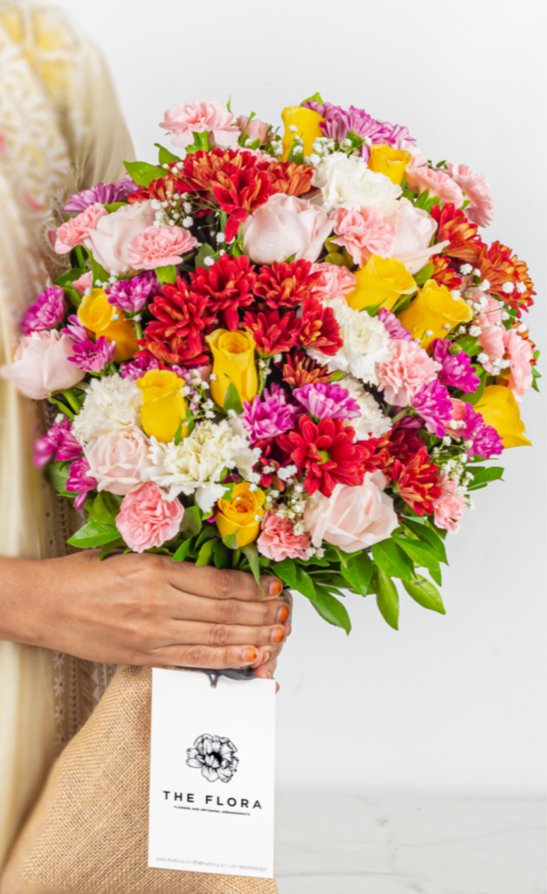 Bouquet of colorful flowers held by a person with 'The Flora' brand label.
