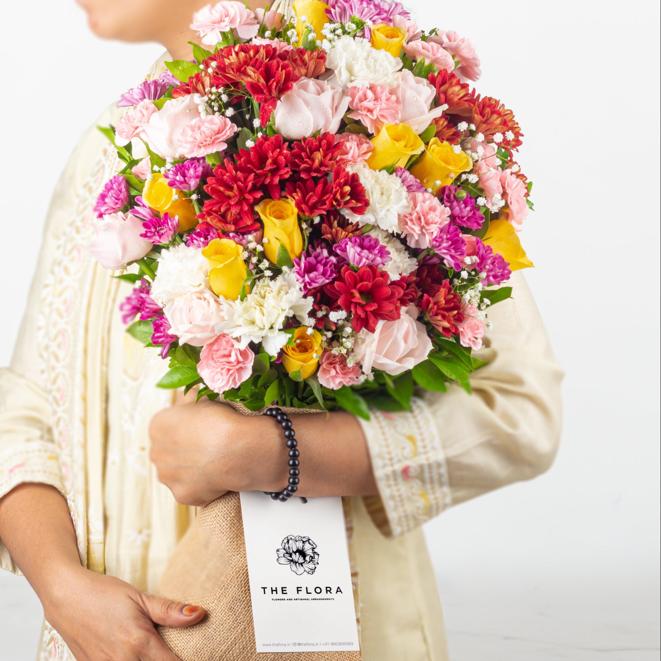 Person holding a colorful bouquet of flowers with 'The Flora' label.
