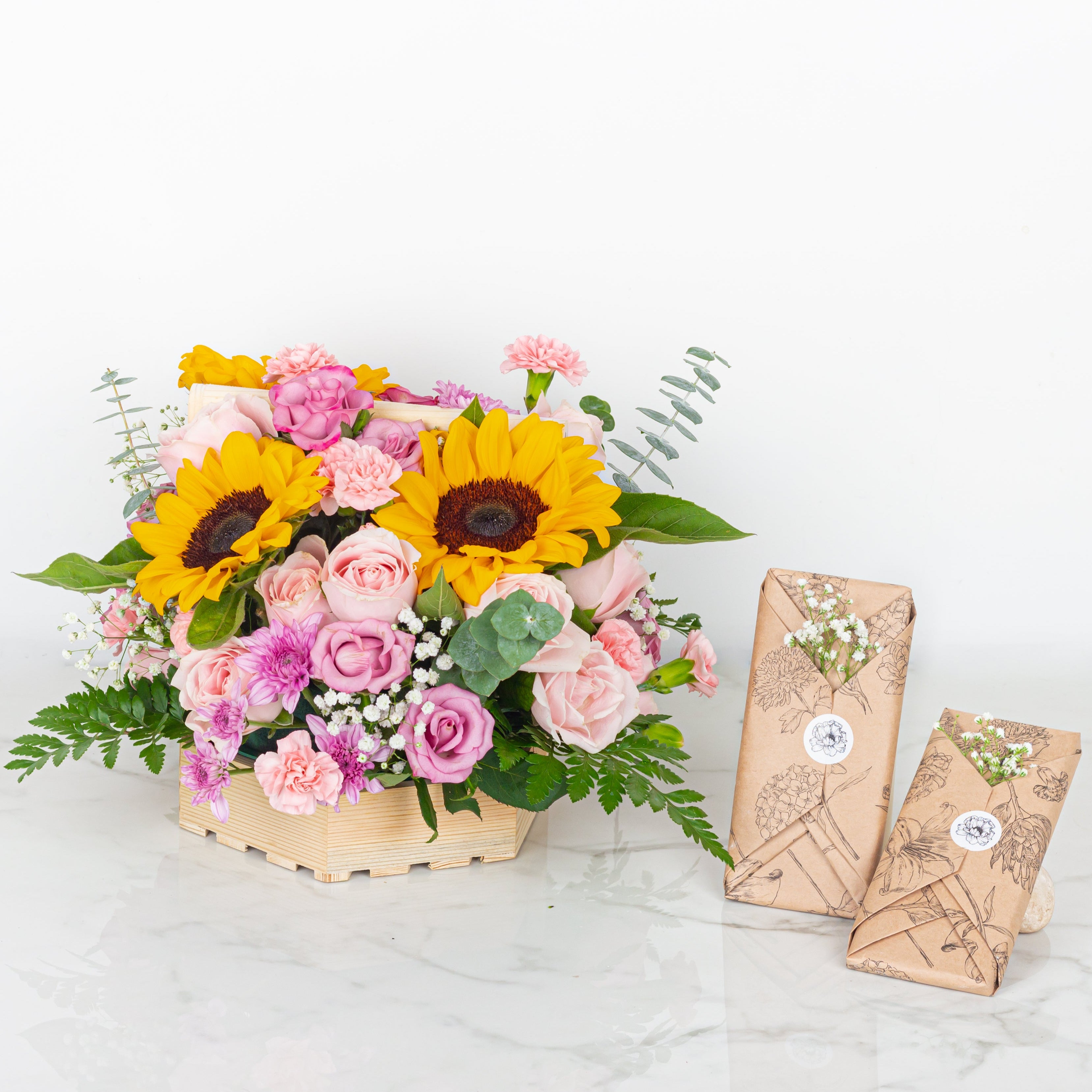 Bouquet of flowers with sunflowers and pink roses, accompanied by two wrapped gifts on a white background.