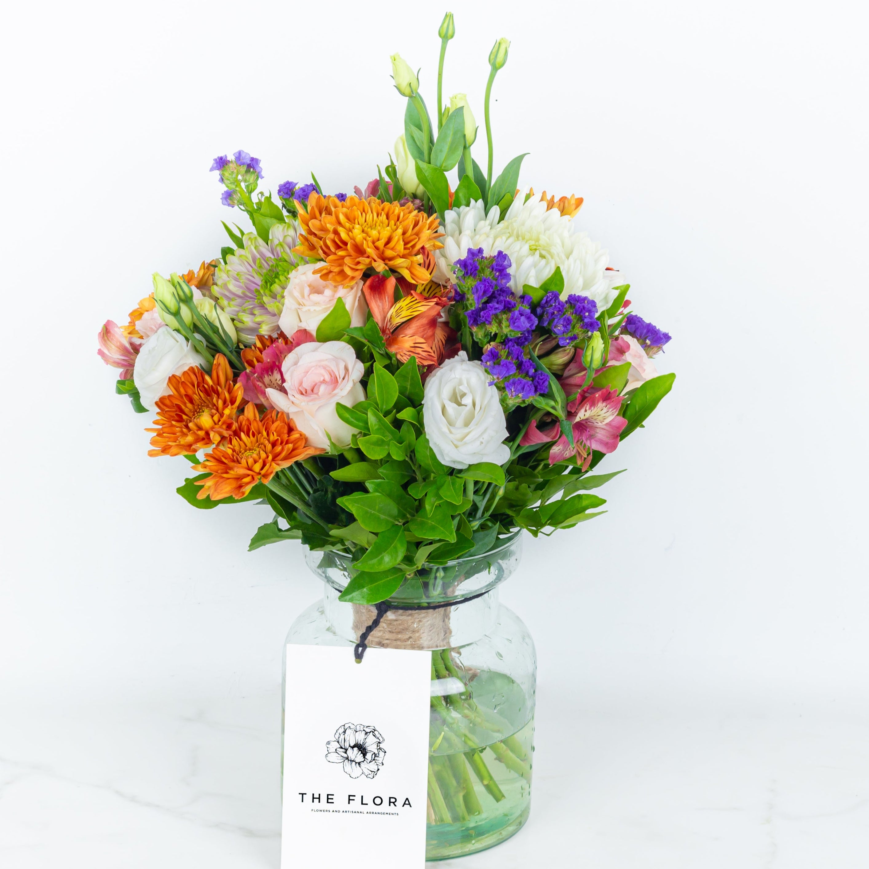Colorful bouquet of flowers  in glass vase with 'The Flora' label called Guardian Grace with Alstroemeria, Lisianthus , Disbud Chrysanthemums, Blue Statice and Roses. Online artisanal bouquets with same day delivery in sustainable packaging at www.theflora.in