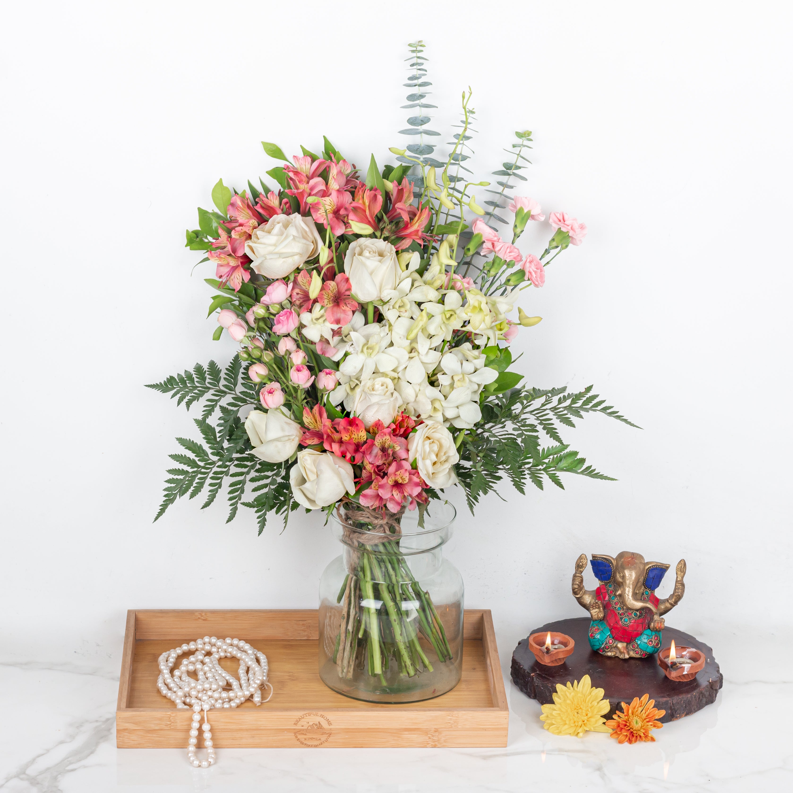 Bouquet of flowers in a glass vase on a wooden tray with decorative items on a white background